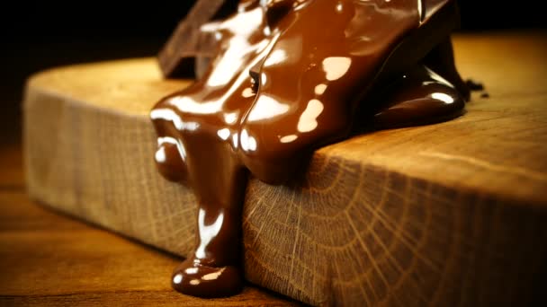 Des morceaux de chocolat noir sont versés avec du chocolat fondu. Le chocolat liquide se propage et coule sur une planche de bois — Video