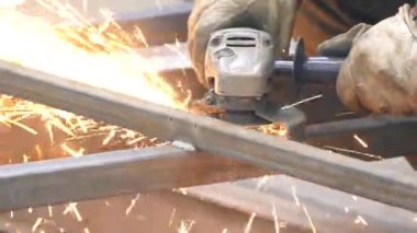Bir kişi bir öğütücü ile çalışır. Fabrikada kesim çelik yapılar. Dışarı güzel kıvılcımlar