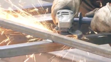 Bir kişi bir öğütücü ile çalışır. Fabrikada kesim çelik yapılar. Dışarı güzel kıvılcımlar