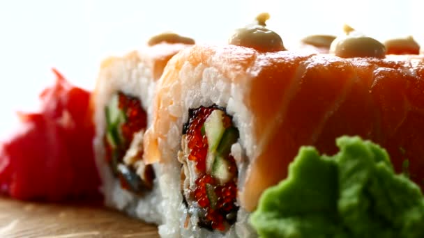 Sushi saporiti e appetitosi. Sushi con fette di salmone e cetrioli freschi. Lo zenzero rosso e il wasabi verde su un'asse di legno sono stati serviti a sushi. Sushi drago rosso — Video Stock