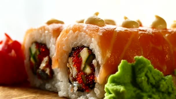 Chutné a chutné sushi. Sushi s plátky lososa a čerstvé okurky. Červený zázvor a zelené wasabi na dřevěné desce byly podává k Suši. Suši červený drak — Stock video