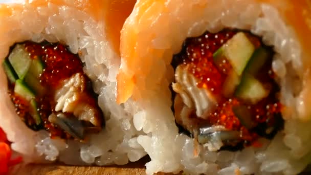 Sushi saboroso e apetitoso. Sushi com fatias de salmão e pepinos frescos. O gengibre vermelho e wasabi verde em uma tábua de madeira serviram-se ao sushi. Dragão vermelho Sushi — Vídeo de Stock