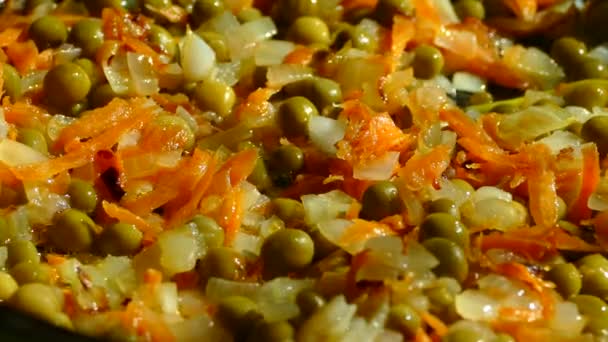 In einer Pfanne aus Zwiebeln und Karotten anbraten. Grüne Erbsen und gefrorene rote Paprika in die Pfanne geben. — Stockvideo