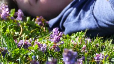 Güzel kız çimenlerin üzerinde mavi çiçeklerle uzanarak rahatlıyor. Güneşli bir bahar gününde bir kız dinleniyor ve gülümsüyor. Saçlar hafif bir esintiyle duyulur..