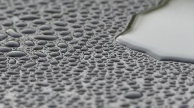 Siyah bir yüzeyde güzel su damlaları. Suyun yoğunluğu karanlık bir düzlemde toplandı. Çiğ tanesinin yansıması.