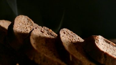 Kesme tahtasının üzerinde dilimlenmiş taze ekmek var. Karanlık arka planda siyah ekmek balıkları. Fırından fırında ekmek..