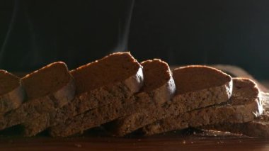 Kesme tahtasının üzerinde dilimlenmiş taze ekmek var. Karanlık arka planda siyah ekmek balıkları. Fırından fırında ekmek..