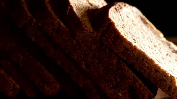 スライスした新鮮なパンはカッティングボードの上にあります 黒いパンは暗い背景に魚を飼っています パン屋から焼いたパン — ストック動画