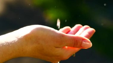 Su damlaları elde toplanır. Bir dağ çeşmesinden su iç. Çevre dostu su. Güneşin arka planına düşer.