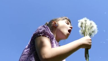 Bir kız mavi gökyüzüne karahindiba ile bir buket üflüyor. 