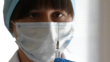 Doktor enjeksiyon için bir şırınga hazırlıyor. Hemşire ilacı bir şırıngada aldı. Hastalığın ilaçlarla tedavi edilmesi. Maske ve şapka takan bir tıp asistanı..