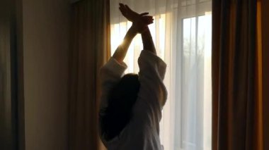 Beyaz önlüklü bir kız perdeleri açıyor. Sabahları pencerenin yanında uzanırım. Günaydın güneşli ve mutlu sabahlar. İyi bir günün başlangıcı.