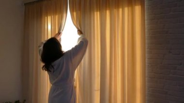 Beyaz önlüklü bir kız perdeleri açıyor. Sabahları pencerenin yanında uzanırım. Günaydın güneşli ve mutlu sabahlar. İyi bir günün başlangıcı.