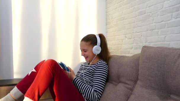 Menina Sorri Olha Para Smartphone Com Fones Ouvido Ouve Música — Vídeo de Stock