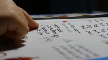 Küçük çocuk okumayı öğreniyor. Kitaptaki bir sayfaya parmak basar.