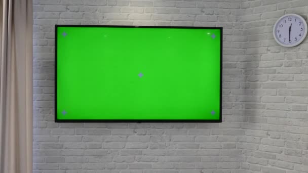 Uma televisão de ecrã verde está pendurada na parede da sala de estar. Contra o fundo de uma parede de tijolo . — Vídeo de Stock