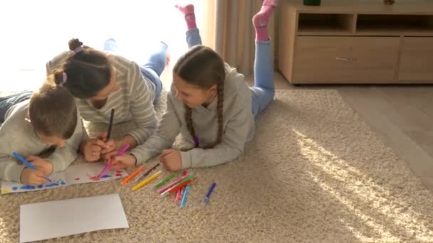 家庭で幸せな家族 女の子と男の子 子供たちとお母さんはマットの上で横になって遊ぶ フェルト先端のペンと鉛筆で描く 娘と息子 — ストック動画