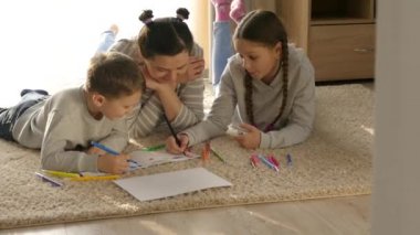Evde mutlu bir aile. Kız ve erkek. Çocuklu annem paspasın üzerinde yatıyor. Keçeli kalem ve kalemlerle çizmek için. Küçük kız ve oğlu..