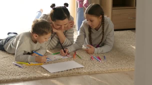 家庭で幸せな家族 女の子と男の子 子供たちとお母さんはマットの上で横になって遊ぶ フェルト先端のペンと鉛筆で描く 娘と息子 — ストック動画