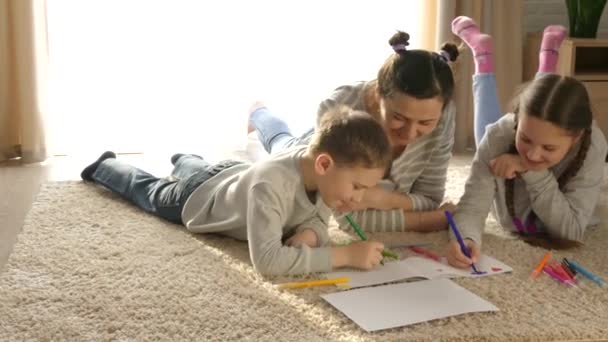 家庭で幸せな家族 女の子と男の子 子供たちとお母さんはマットの上で横になって遊ぶ フェルト先端のペンと鉛筆で描く 娘と息子 — ストック動画