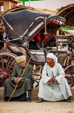 Edfu, Mısır - Ocak 2019: Mısır halkı, Edfu Tapınağı etrafında konuşan eski Mısırlılar. Turistleri Nil gezilerinden Edfu Tapınağı 'na taşımak için kullandıkları arabalar arkada görünüyor.