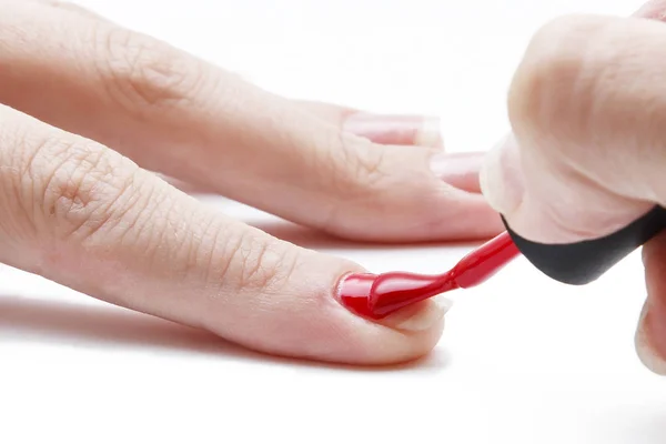 Aplicando esmalte de uñas rojo a la uña sobre un fondo blanco — Foto de Stock