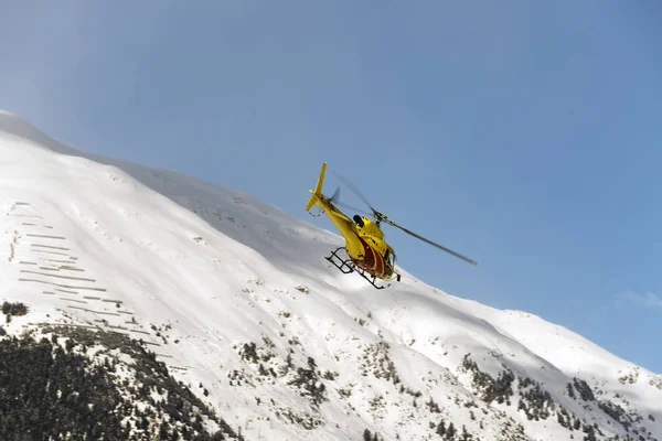 A yellow helicopter flying up in the air over the small town in Engadin St moritz Switzerland in the alps for sightseeing in winter