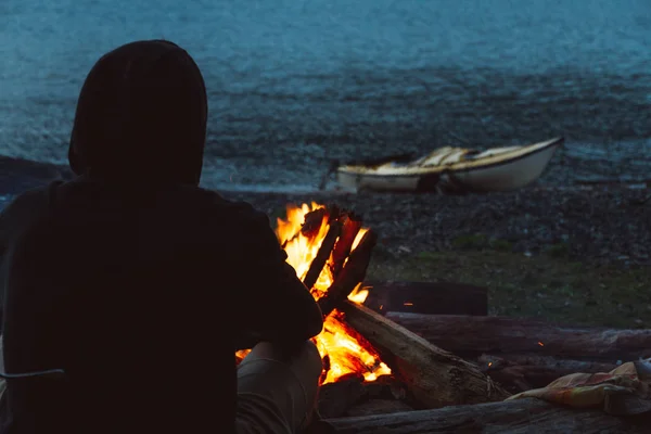 夜のビーチでキャンプファイヤーの近くのカヤックを持つ男 — ストック写真