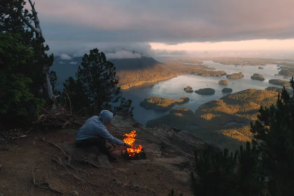 Man sitting on the rim with campfire above coastal view with isl — Stock Photo, Image