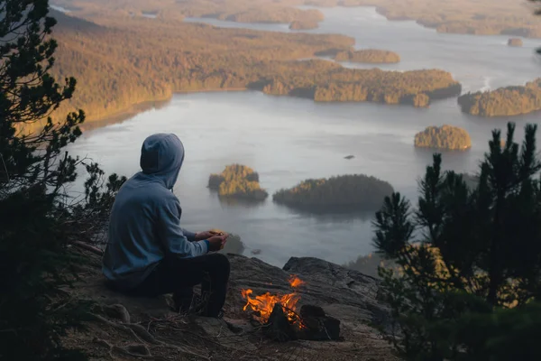 Homem sentado na borda com fogueira acima da vista costeira com isl Imagens De Bancos De Imagens