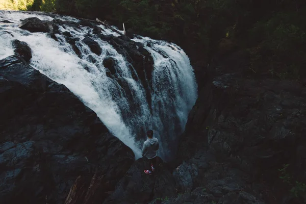 Homem de pé na borda do penhasco na floresta com cachoeira — Fotografia de Stock
