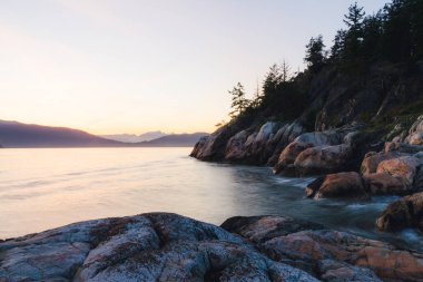 Kenarı kayalıklarla ve arka plan dağlarda günbatımı