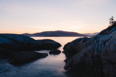 Kenarı kayalıklarla ve arka plan dağlarda günbatımı