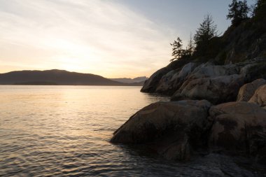 Kenarı kayalıklarla ve arka plan dağlarda günbatımı