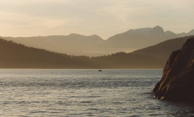 Kenarı kayalıklarla ve arka plan dağlarda günbatımı
