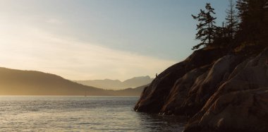 Kenarı kayalıklarla ve arka plan dağlarda günbatımı