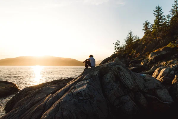 而日落海滩附近的岩石上坐着的人 — 图库照片
