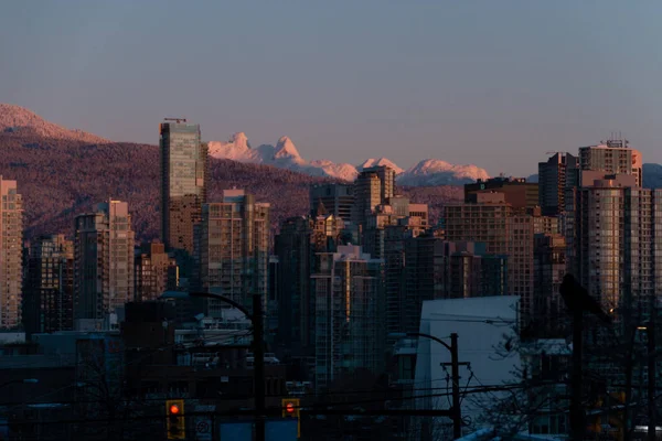 Paisagem urbana de inverno com montanhas e nascer do sol iluminando buildin — Fotografia de Stock