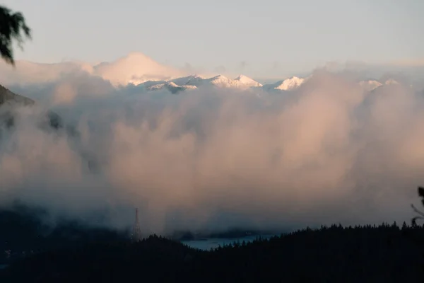 Montagne innevate visibili sopra le nuvole con lago sotto — Foto Stock