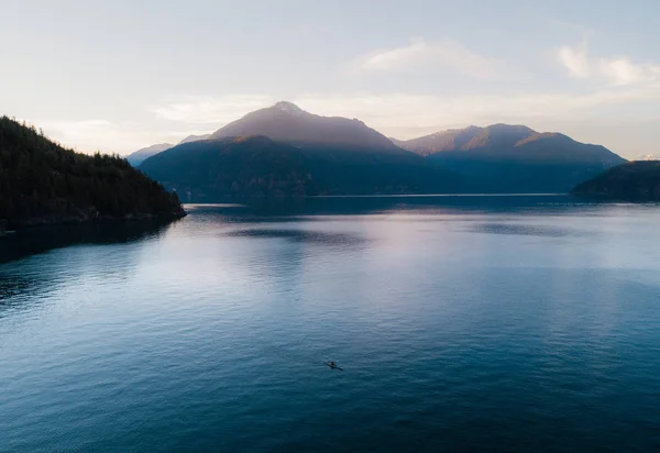 Tiro aéreo de caiaque no lago com montanhas enquanto o pôr do sol — Fotografia de Stock