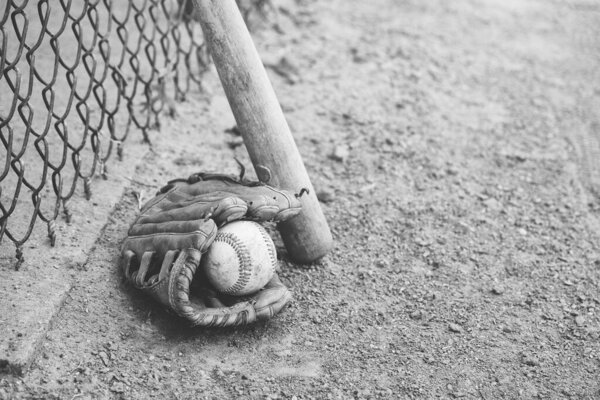 Baseball in old glove with bat on field in black and white.