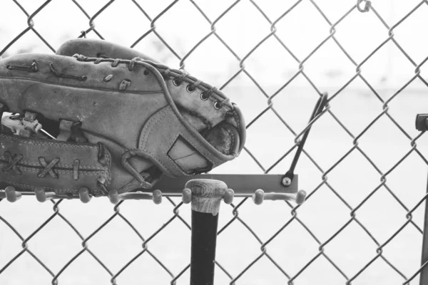 野球手袋とバットの閉鎖チェーンリンクダグアウトフェンスの背景で黒と白 — ストック写真