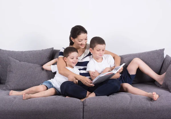 Мати читає цікаву книгу з синами дивана. — стокове фото