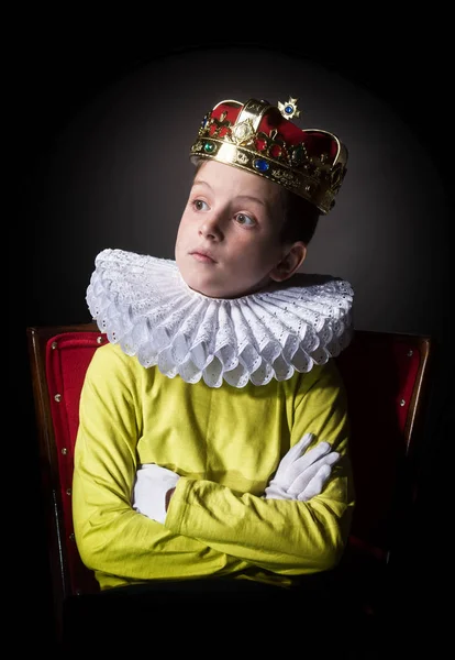 Gekroond jongen zitten in een leunstoel — Stockfoto