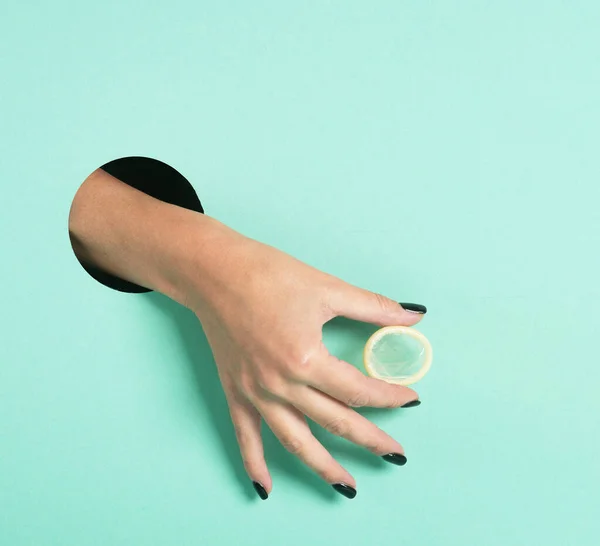 Frauenhände halten Kondom durch ein Loch. Safe Anonymous Sex Konzept. isoliert auf Neon Mint Hintergrund. — Stockfoto