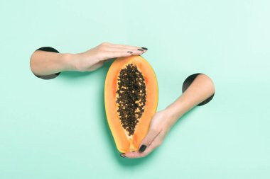 Kadın elleri taze papaya 'yı neon arkaplanda bir delikten tutuyor. Asgari yaratıcı izole kavram.