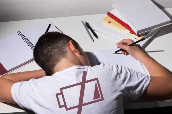 Набридлий і втомлений хлопчик робить домашнє завдання на білому столі у своїй кімнаті. Концепція шкільного хлопчика . — стокове фото