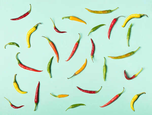 Red, green and yellow hot chili peppers in flat lay style. Pattern on neon mint background.