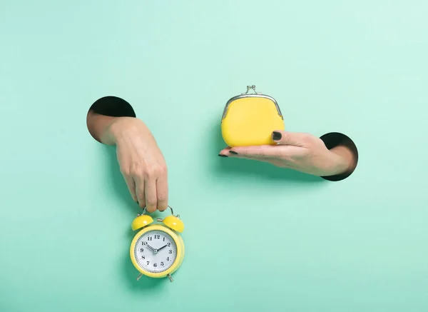 Female hands hold alarm clock and wallet through a hole on neon mint background. Minimalistic creative isolated time is money concept.