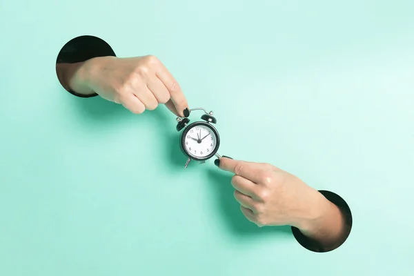 Tangan wanita memegang jam alarm melalui lubang di neon mint latar belakang. Konsep kreatif minimalis. — Stok Foto